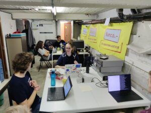 De ULYSSIS kelder. Zes mensen zitten aan twee tafels met laptops, kabels en servers.